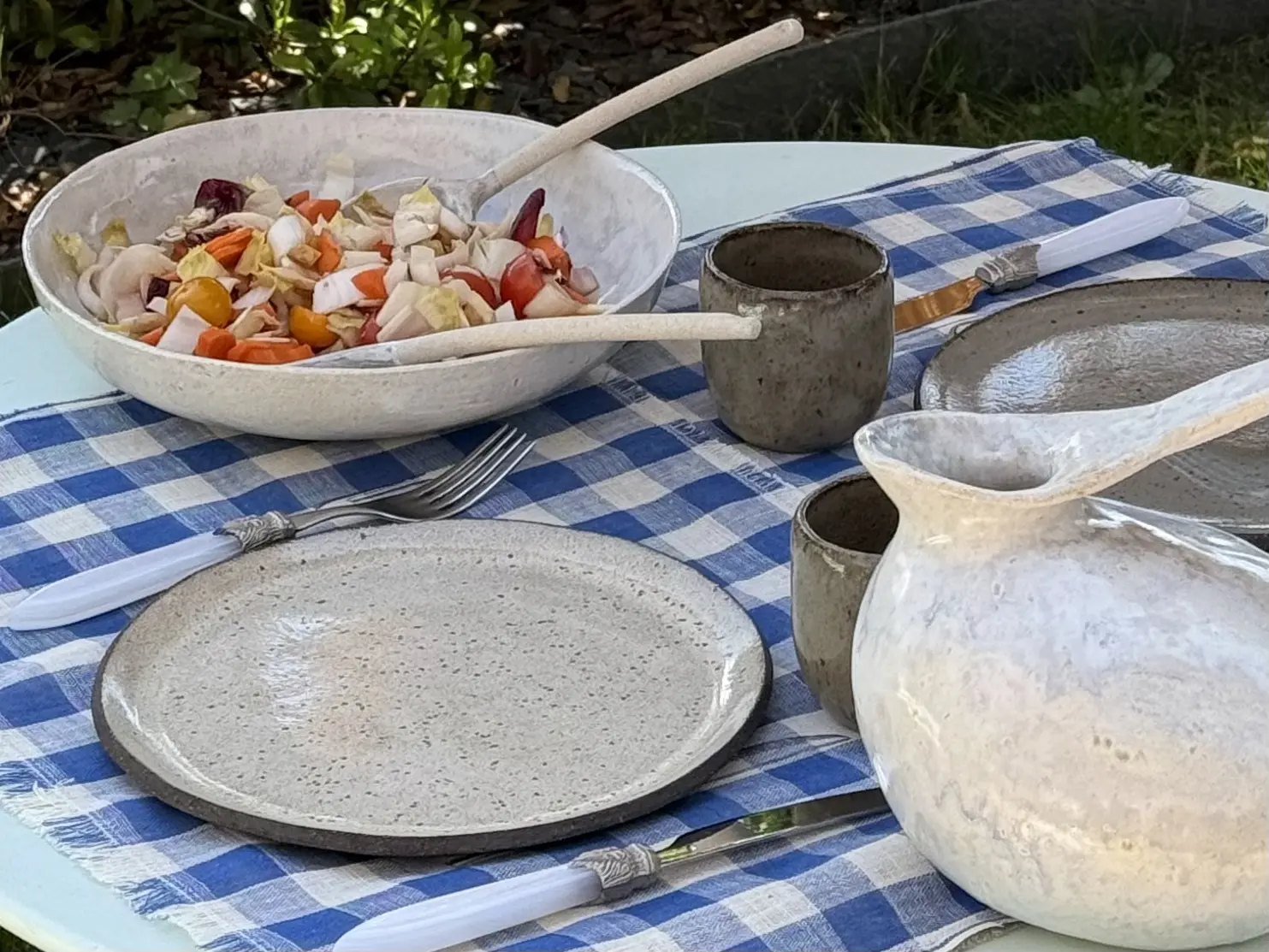 Vaisselle artisanale en grès sur une table à l'extérieur.