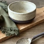 Bol Demba crème en grès noir artisanal posé sur une table à côté de la cuillère Bintou