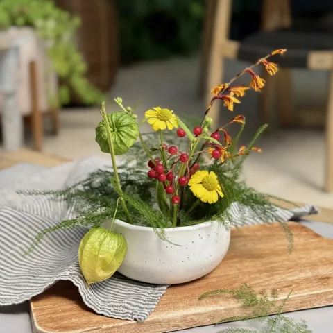 Pique-fleurs Alba en céramique artisanale avec des fleurs posé sur une table à l'extérieur.