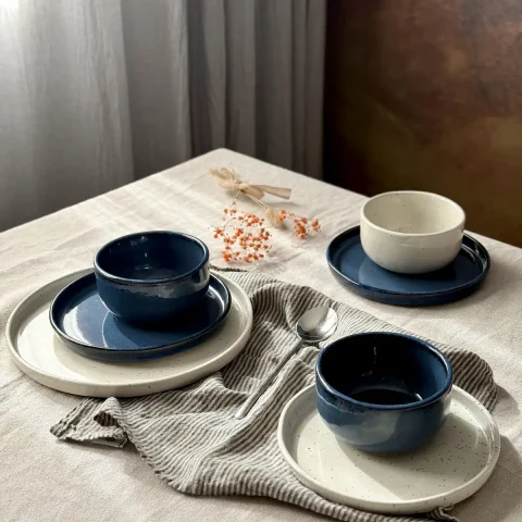 Bols DEMBA bleu profond et blanc pyrité sur des assiettes ELIA, disposés sur une table dressée.