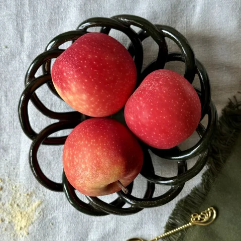 Coupe à fruits Zélie en grès vert profond avec trois pommes rouges.