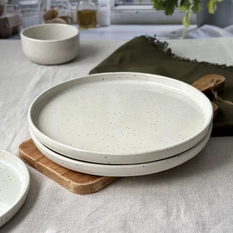Deux grandes assiettes ELIA blanc pyrité empilées sur une table.