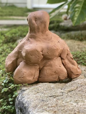 Petite statuette en grès façonnée par un enfant, céramique artisanale posée dans le jardin.