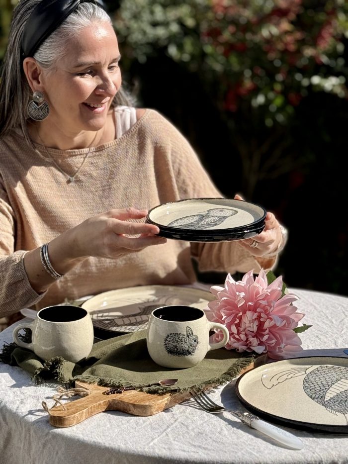 Lis céramiste prend une petite assiette en grès de la collection Terre sauvage en céramique artisanale sur une table dressée dans le jardin.